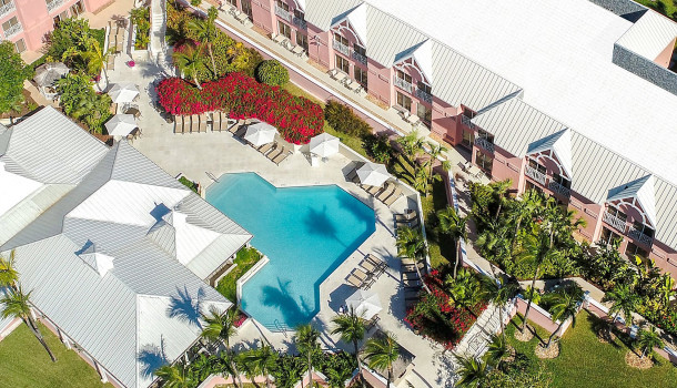 Aerial view of property with pink buildings enclosing pool area with white loungers