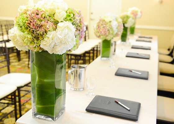 Long rectangular table set with flower arrangements & notepads