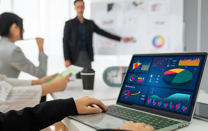 closeup view of a laptop with graphics on the screen and a blurry guy and lady at the back