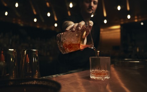 hand pouring cocktail onto a short glass