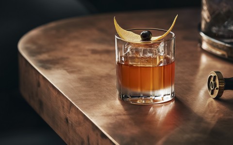 single cocktail glass with orange peel garnish on a table
