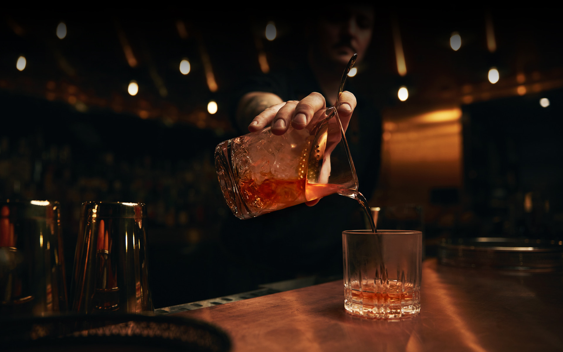 dark version of a hand pouring a cocktail into a glass