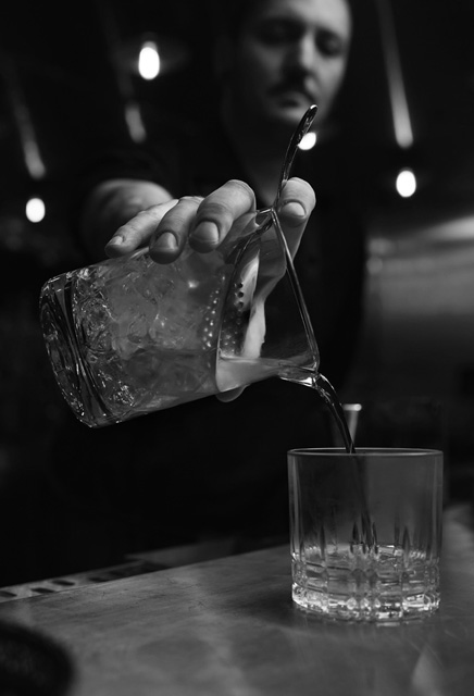 person pouring a shaken drink into cocktail glass black and white