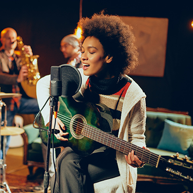 woman sitting on a stool and singing while playing guitar on stage