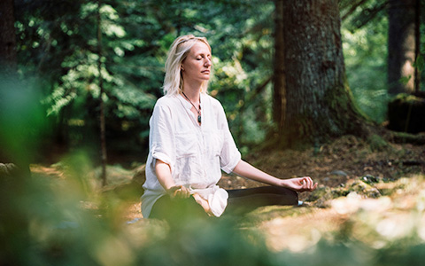 woman meditating outside in wooded area