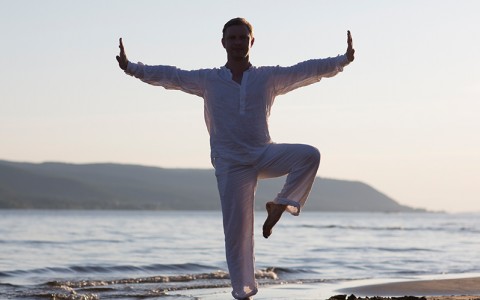 man posing on beach along shoreline balancing on one leg in yoga pose