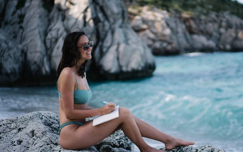 fit woman sitting on rocks along the shoreline journaling