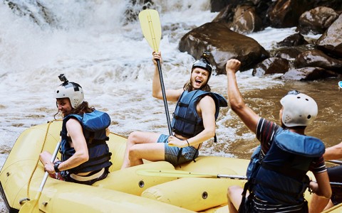 three people white water rafting wearing helmets and life vests