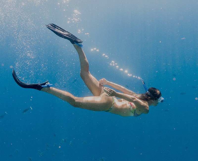 woman swimming in deep water wearing snorkeling gear and swimming fins