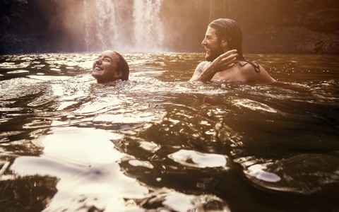 man and woman emerging from water at bottom of waterfall