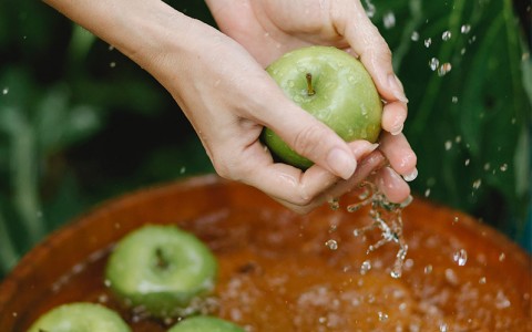 person cleaning a green apple with water 