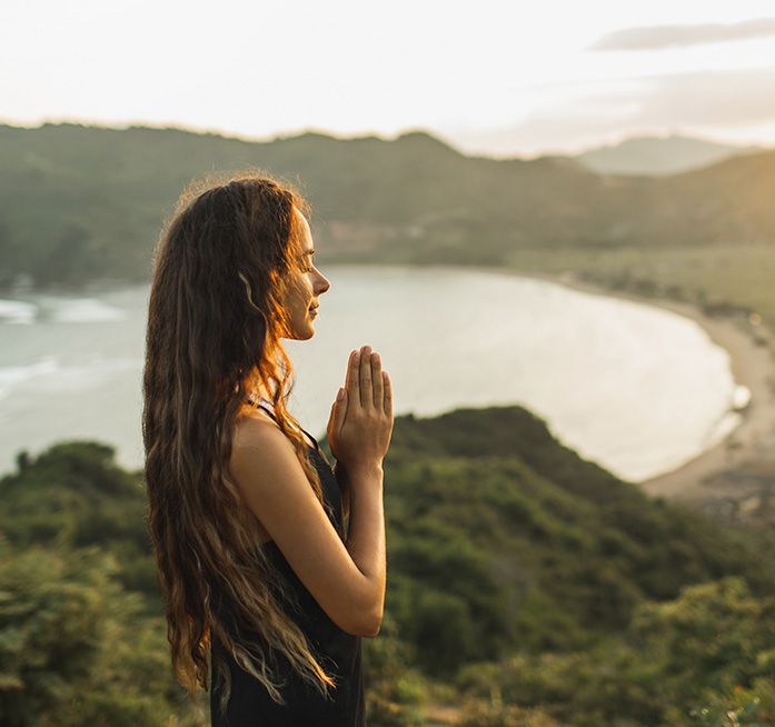 woman meditating outside on a mountain at sunset 