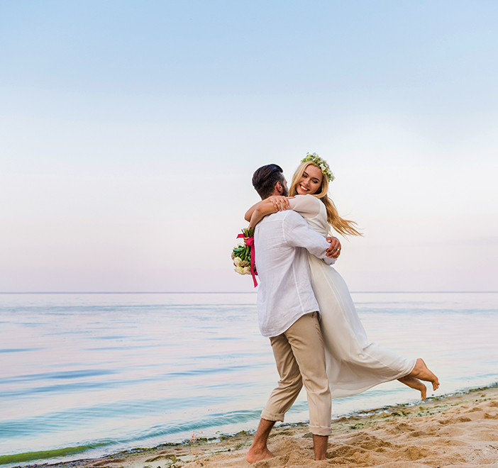 groom lifting his bride up in a hugging embrace on the beach