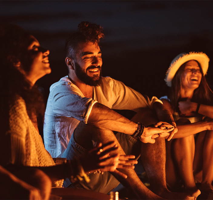 three people sitting in beach in front of a fire