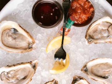 Chilled oysters with two sliced lemons, a fork, hot sauce and dipping marinara sauces