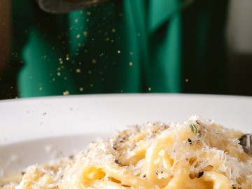 Person grating Parmesan cheese atop of pasta