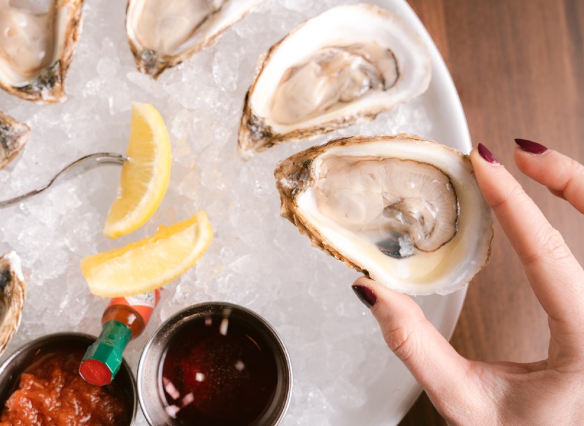 Feminine hand holding an oyster with chilled oysters and sliced lemons in the background