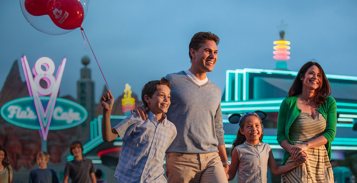 Man, woman and their two kids with neon lighted buildings behind them