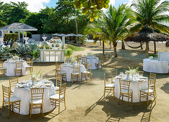 wedding reception tables on the sand with gold chairs and white tablecloths 