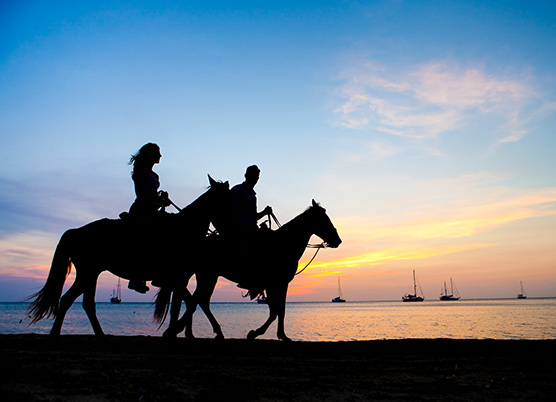 couple riding horses on the beach at sunset