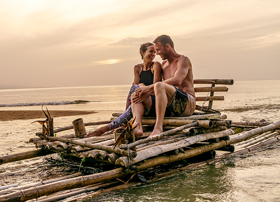 couple sitting on a bamboo raft in the water at sunset