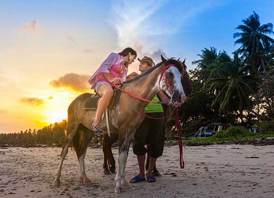 woman sitting on a horse talking to a man on the beach at sunset