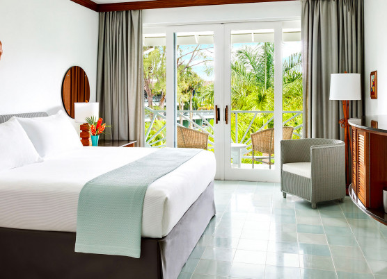 guest room with white linens, light blue quilt draped on bed, light blue tile floors, wood furnishings, and double doors leading to a patio
