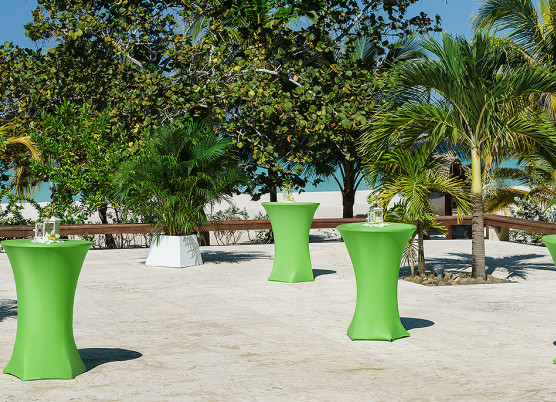 green cocktail tables on a concrete terrace  with palm trees blocking a view of the ocean