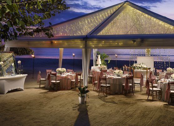 a wedding dining reception on the beach at night covered with a large tent