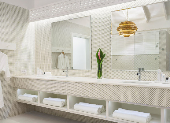 bathroom area with a double sink vanity, shelving underneath with rolled up towels, robes hanging, and two mirrors
