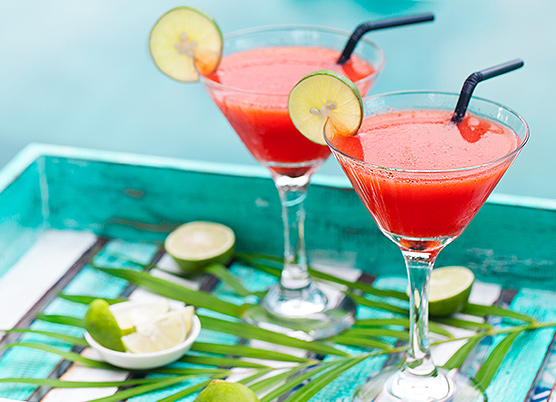 two strawberry and lime cocktails in martini glasses on a blue tray