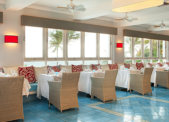 indoor restaurant dining area with bench seating and tan wicker chairs overlooking the ocean