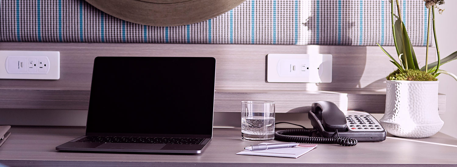 guest room desk area with a laptop, glass of water, phone, pen and paper