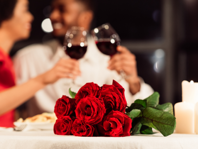 Close up of a bouquet of roses with a couple drinking wine in the background 