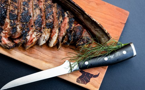 meat cut on a wooden cutting board and a steak knife next to it