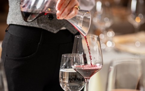 server pouring red wine in a wine glass on a table 
