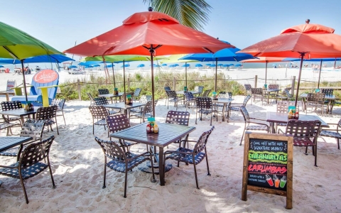 Chalk board offering Cabanaritas next to metallic tables & chairs with umbrellas outside on sand
