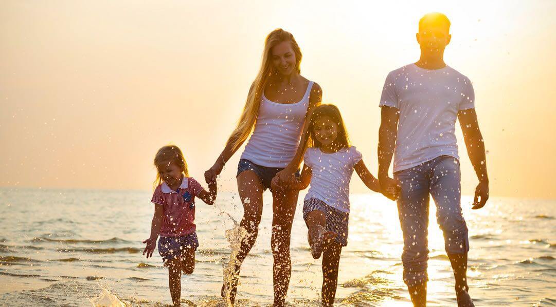 Couple with two kids walking on ocean shore with sun setting in the back