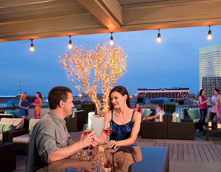 A couple sits together at a table drinking wine on a rooftop terrace