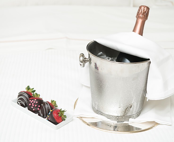 chocolate covered strawberries on a plate next to a champagne bucket on a bed