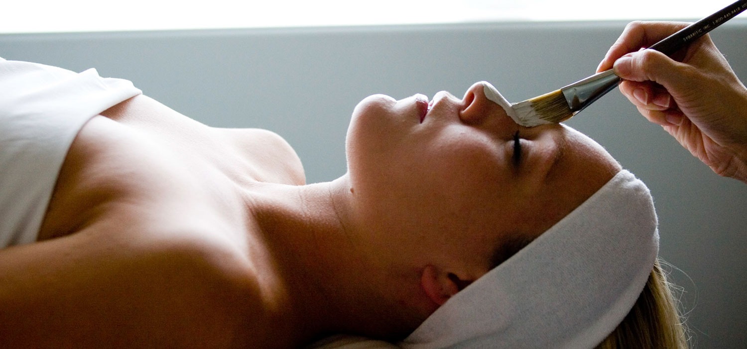 woman laying down for spa treatment getting face mask put on by someone