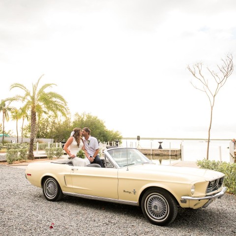 newlyweds sitting in the back of a yellow classic convertible
