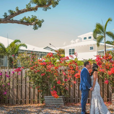 newlyweds kissing in front of bright red flowers