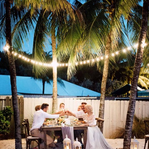 small bridal party having a meal on a table outside with twinkly lights