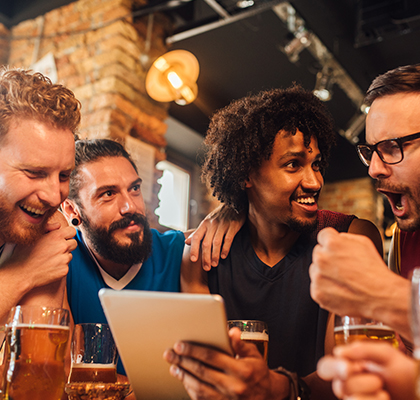 four men drinking beer looking at a tablet