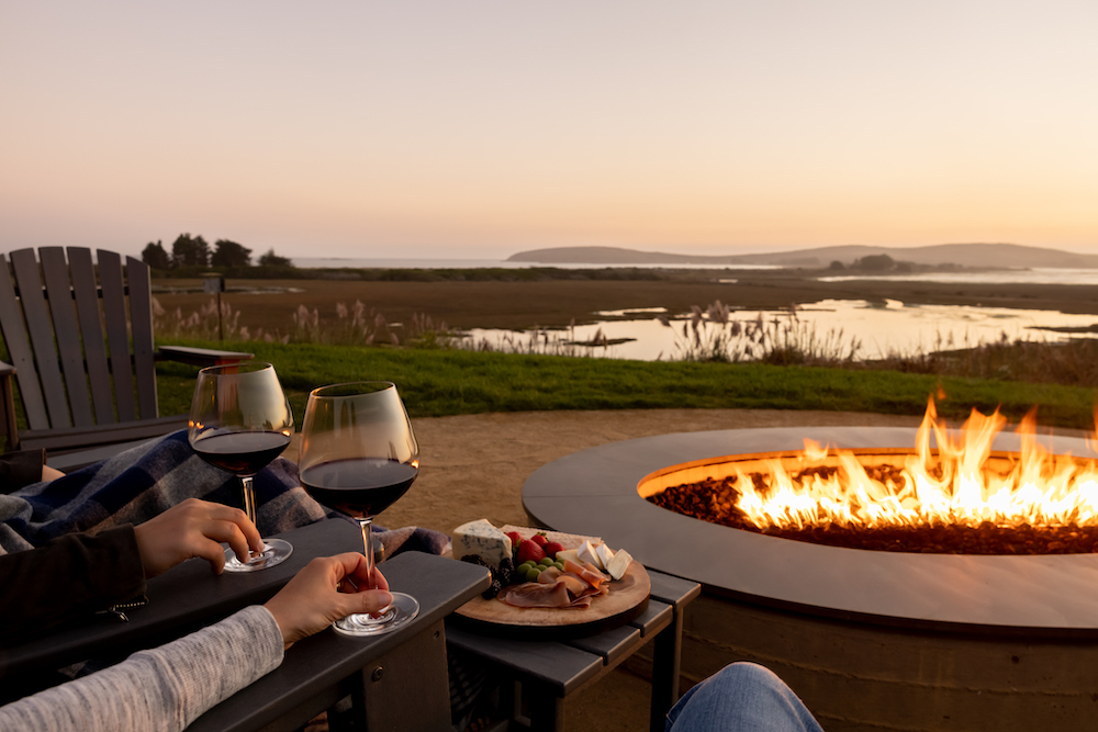 fire pit overlooking the water holding glasses of red wine