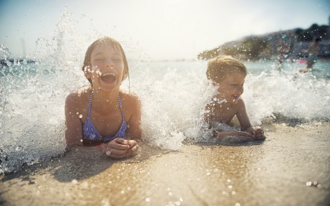 Two kids playing in sand with water splashing over them