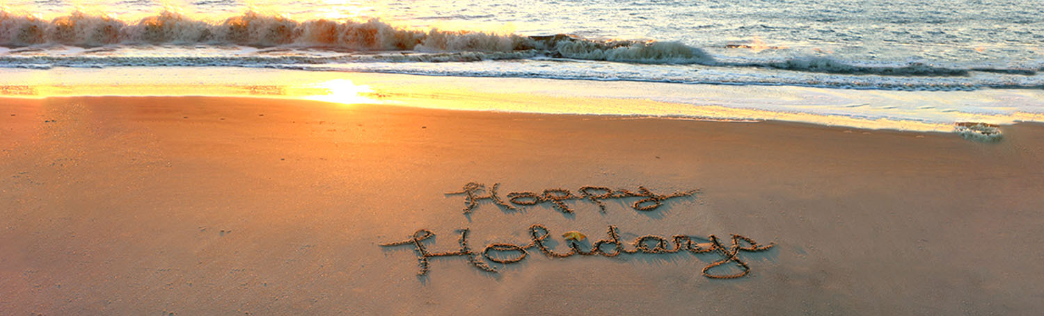 beach with happy holidays written in the sand