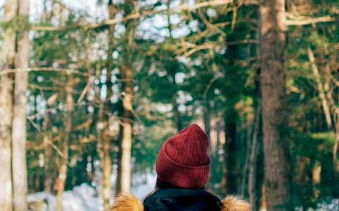woman walking in woods wearing jacket and knit cap in winter
