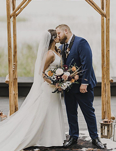 bride and groom kissing underneath a wooden wedding arch
